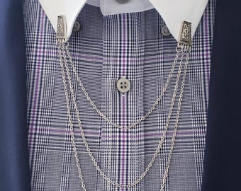 May include: Silver-toned collar chain clipped to a white collared shirt over a plaid shirt. The plaid shirt has a pattern of navy blue, white, and purple. A navy blue blazer is visible on the sides.