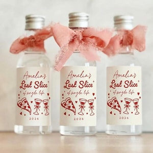 May include: Three clear glass bottles with silver caps, each adorned with a pink ribbon. The labels read "Amelia's Last Slice of single life" with pizza and wine glass graphics, and the year 2026. A charming gift for a bachelorette party.