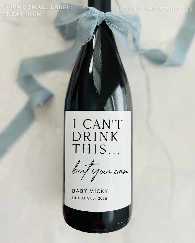May include: A white wine bottle label with black text that reads "I can't drink this... but you can".  The label also includes the text "Baby Micky Due August 2026".