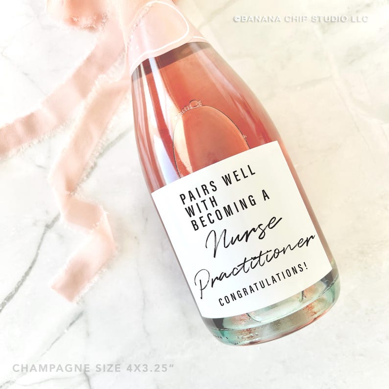 May include: A champagne bottle with a pink label that reads "PAIRS WELL WITH BECOMING A Nurse Practitioner CONGRATULATIONS!". The bottle contains a pink liquid and is decorated with a pink ribbon. The bottle size is approximately 10.16cm x 8.26cm.
