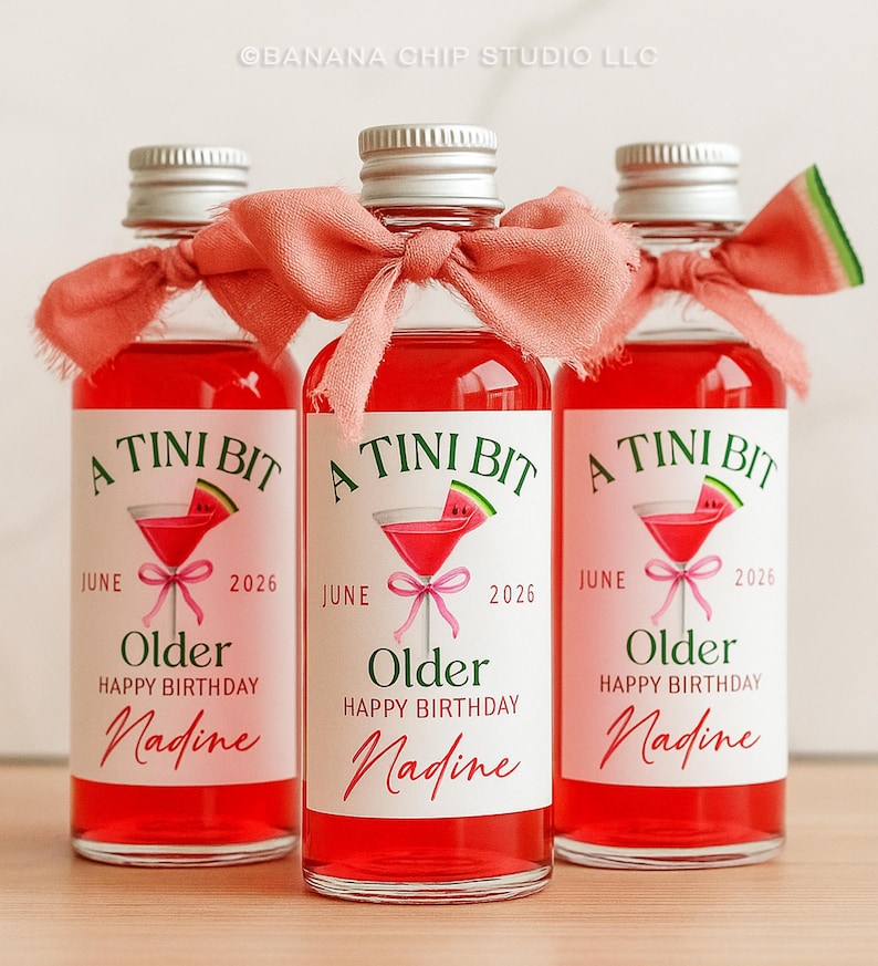 Puede incluir: Tres botellas de vidrio peque&ntilde;as llenas de un l&iacute;quido rojo brillante, cada una con una tapa plateada y una cinta color coral. Las etiquetas dicen "A Tini Bit" con una ilustraci&oacute;n de c&oacute;ctel, "Junio 2026", "Older Happy Birthday Nadine".