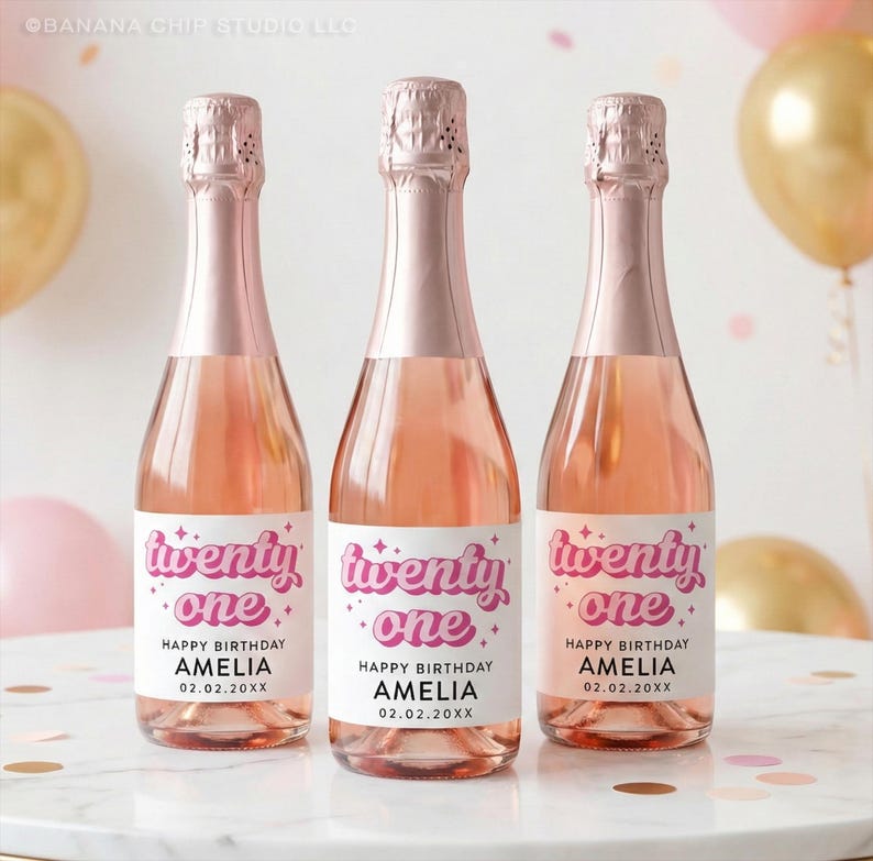May include: Three glass bottles filled with a rose-colored liquid, each featuring a white label with the pink text twenty one, the words HAPPY BIRTHDAY AMELIA, and the date 02.02.20XX. The bottles have metallic rose gold foil neck wraps.