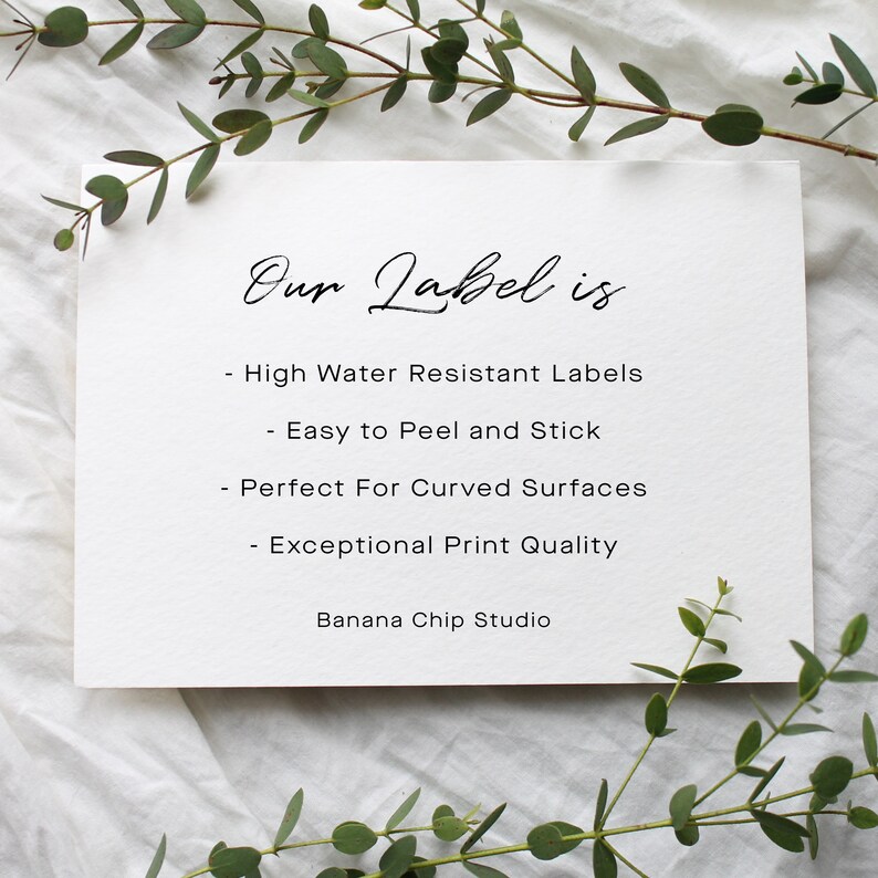 May include: A white card with the text "Our Label is" in elegant script. Below, bullet points list features: high water resistance, easy peel and stick, perfect for curved surfaces, and exceptional print quality. The card is surrounded by greenery.