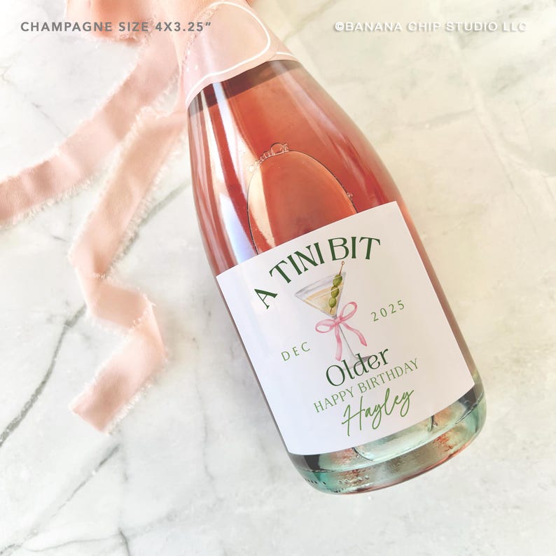 Puede incluir: Una botella de champ&aacute;n con una etiqueta personalizada que dice "A Tini Bit Older Happy Birthday Hayley" con una ilustraci&oacute;n de martini. La botella mide 10,16 x 8,26 cm y tiene una cinta rosa atada alrededor del cuello.