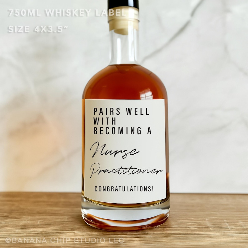 May include: A clear glass whiskey bottle with a white label. The label reads "PAIRS WELL WITH BECOMING A Nurse Practitioner CONGRATULATIONS!". The bottle is filled with amber liquid. The label size is 10.16cm x 8.89cm.