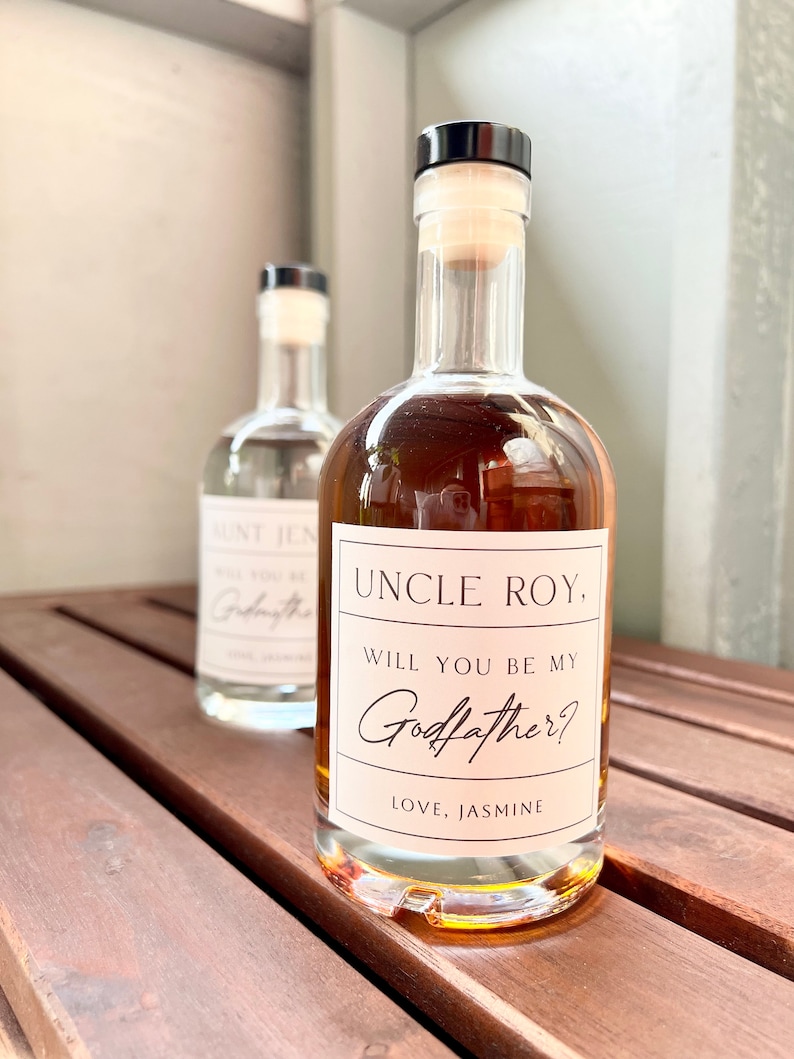 May include: Two glass bottles with cork stoppers. The front bottle has a label reading "UNCLE ROY, WILL YOU BE MY Godfather? LOVE, JASMINE." The second bottle has a label reading "AUNT JEN, WILL YOU BE MY Godfather?"