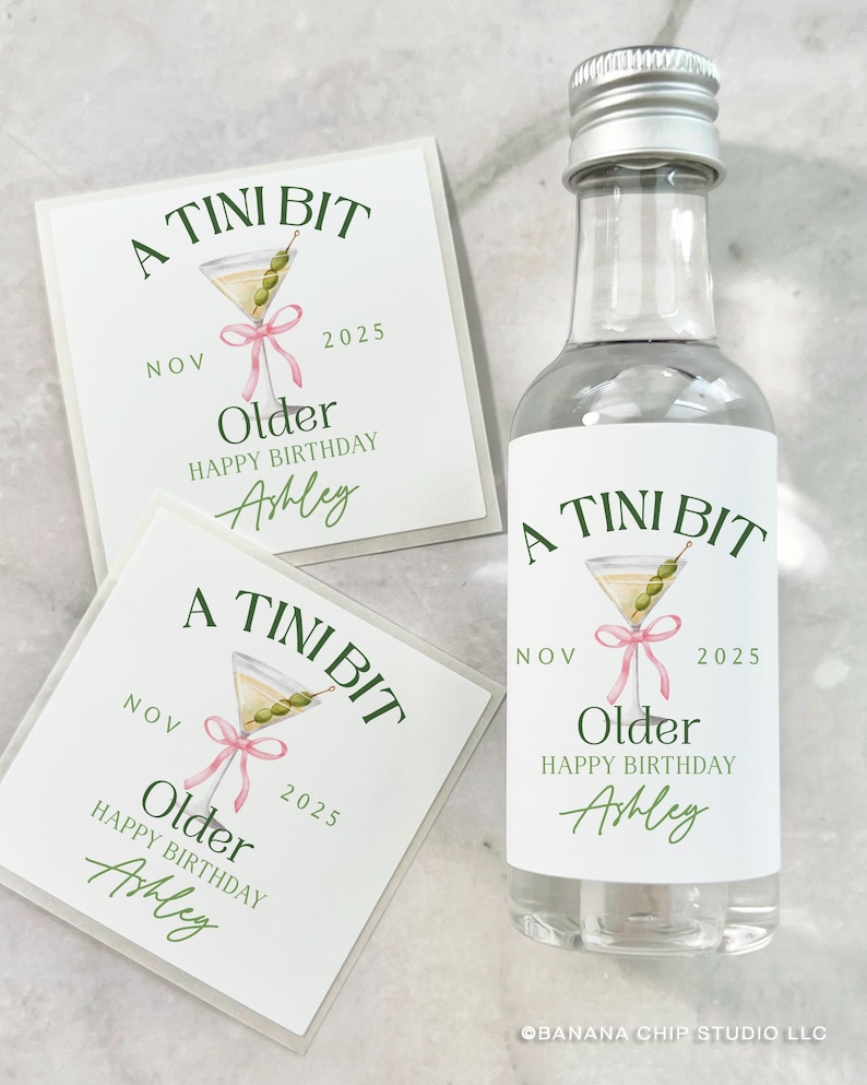 Puede incluir: Una botella de vidrio transparente con tapa plateada y una etiqueta que dice "A Tini Bit Older Happy Birthday Ashley" con una ilustraci&oacute;n de martini. Dos tarjetas a juego est&aacute;n junto a la botella.