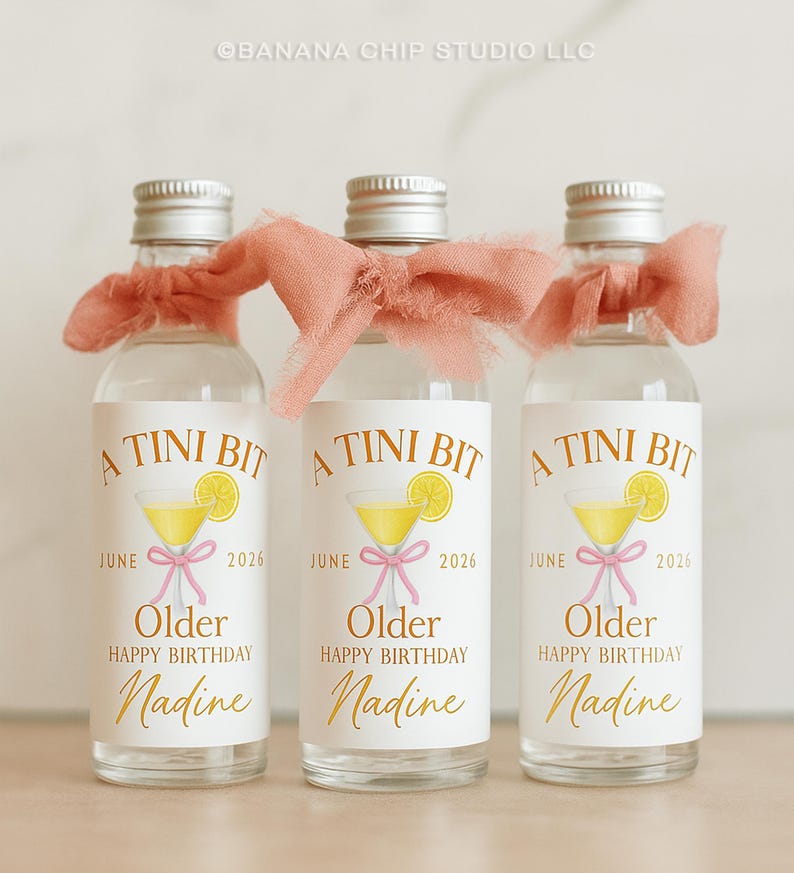Puede incluir: Tres botellas de vidrio transparente con tapas plateadas, cada una adornada con una cinta color melocot&oacute;n. Las etiquetas dicen "A Tini Bit" con una ilustraci&oacute;n de c&oacute;ctel, el nombre "Nadine" y "Feliz Cumplea&ntilde;os". Para un cumplea&ntilde;os en junio de 2026.