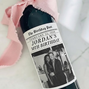 May include: A dark green wine bottle with a custom label that reads "The Birthday Post" and "Jordan's 30th Birthday." The label includes a black and white photo of a couple. A pink ribbon is tied around the bottle's neck.