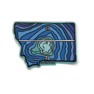Puede incluir: Una pegatina azul y verde con un diseño de mapa topográfico de Montana. La pegatina tiene los números 23 y 26 y el texto "@artbychristel".