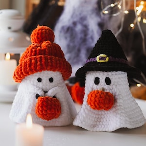 May include: Two crocheted ghost ornaments, one wearing a black witch hat and the other a bright orange knit hat. Both ghosts are holding orange yarn pumpkins in their hands.