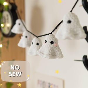 Könnte beinhalten: Eine Girlande aus weißen, flauschigen Geisterdekorationen mit schwarzen Augen und rosigen Wangen, auf einer schwarzen Schnur. Die Geister hängen vor einem hellen Hintergrund, mit dem Text "NO SEW" in einer weißen Box. Gelbe Sterne sind verstreut.