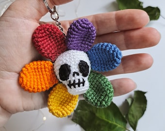 May include: A rainbow crocheted flower keychain with a white skull in the center. The keychain has a silver ring.