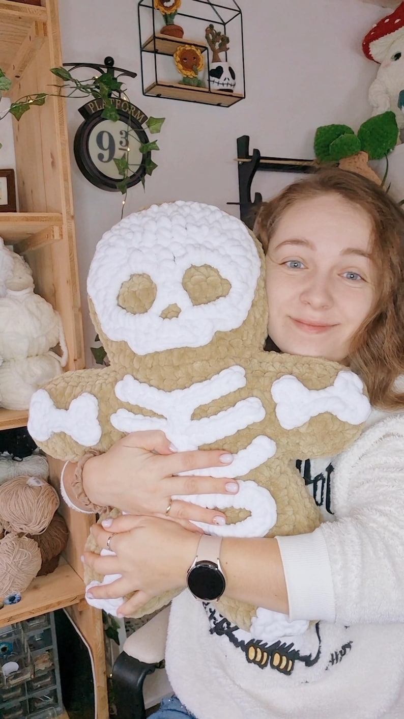 May include: A plush, tan-colored skeleton-shaped pillow with white bone detailing. The pillow is soft and cuddly, perfect for Halloween or spooky decor. The skull and bones are clearly defined, creating a fun, whimsical design.