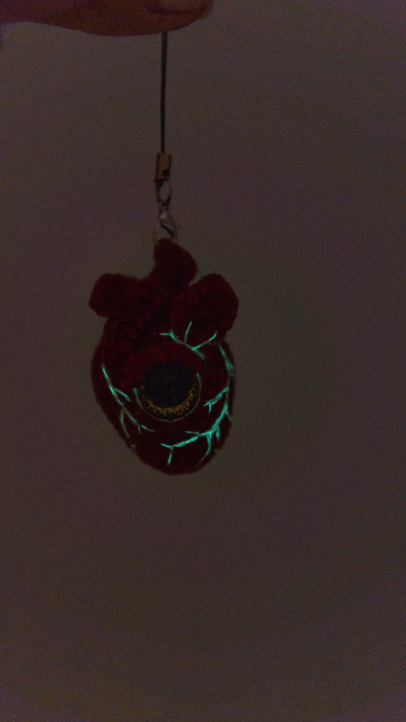 May include: A red plush heart-shaped keychain with a glowing green eye and veins. The keychain is hanging from a black string.