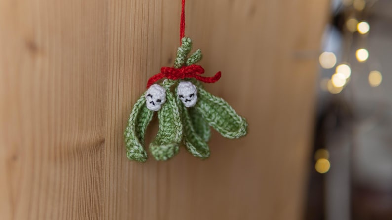 Pu&ograve; includere: Una decorazione di vischio all'uncinetto con un nastro rosso e facce bianche. Il vischio &egrave; verde e ha una forma tradizionale.