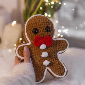 May include: A handmade brown gingerbread man plushie with a red bow tie and white accents. The plushie has black button eyes and is outlined in white. A festive holiday decoration.
