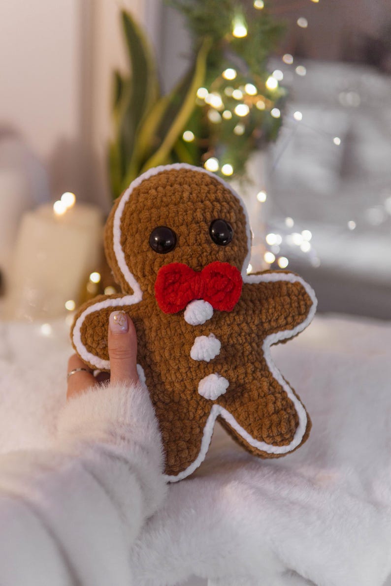 May include: A handmade brown gingerbread man plushie with a red bow tie and white accents. The plushie has black button eyes and is outlined in white. A festive holiday decoration.