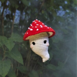 May include: A crocheted mushroom toy with a red and white cap and a white body. The mushroom has a cute face with black eyes and a small smile.