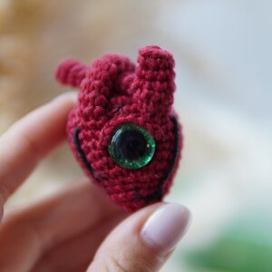 May include: A crocheted red heart with a green eye.