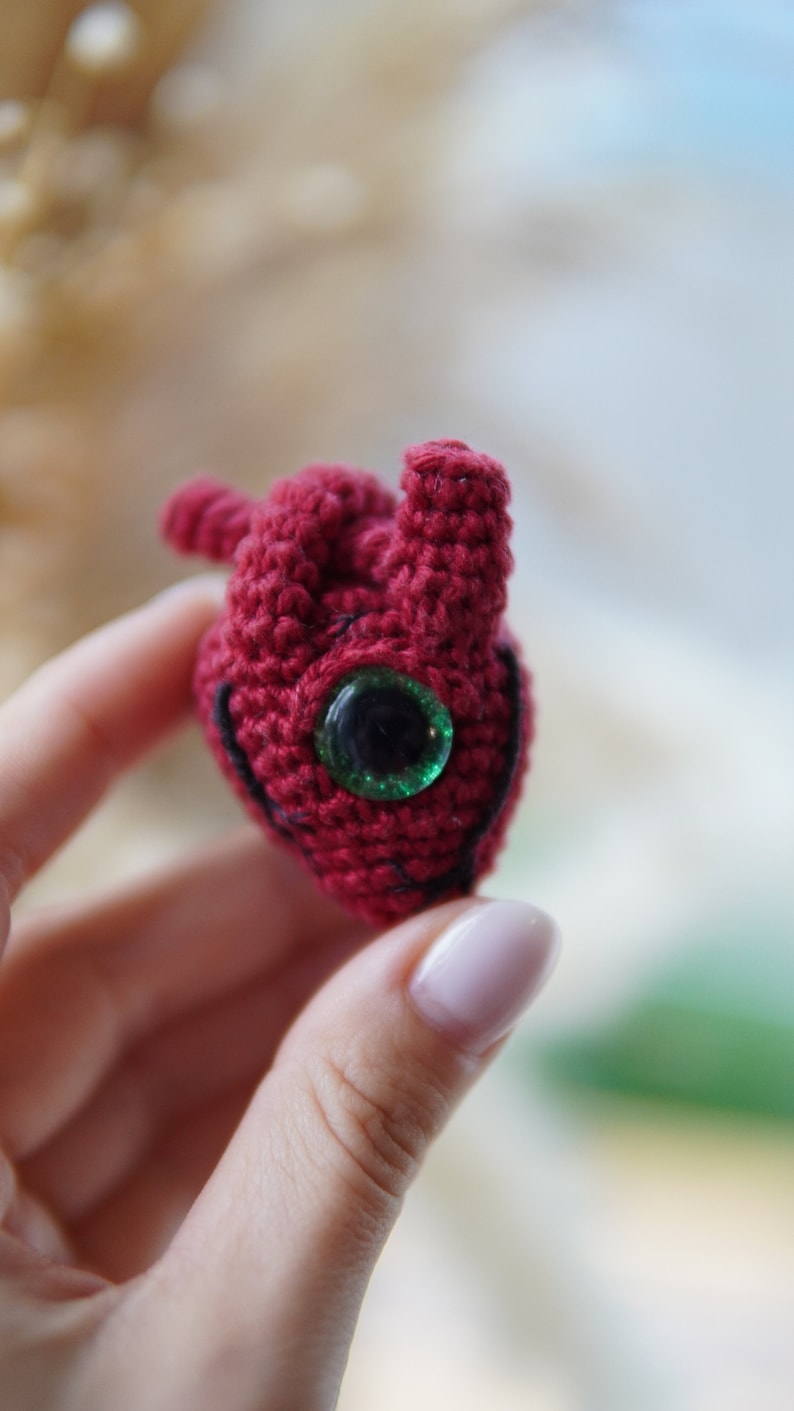 May include: A crocheted red heart with a green eye.