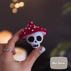 May include: A crocheted skull wearing a red mushroom cap with white spots. The skull has black eye sockets and a stitched mouth. The image includes the text "No Sew".