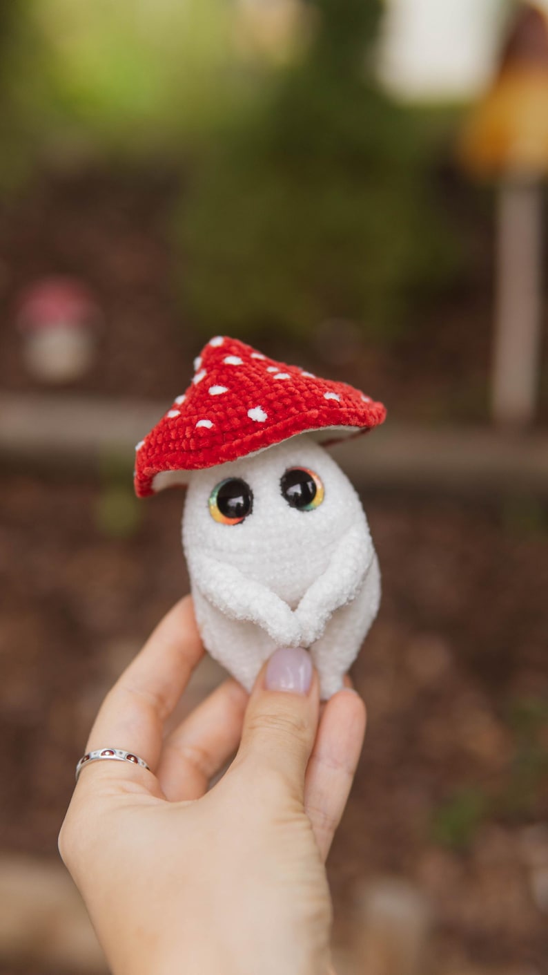 以下が含まれることがあります： 白いキノコのぬいぐるみ。赤い帽子に白い水玉模様。虹色の虹彩を持つ大きな目と小さな腕があります。子供向けの柔らかいおもちゃです。