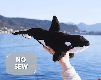 May include: A black and white crocheted orca plush toy featuring a dorsal fin, side flippers, and a tail fluke. The plush has a white patch near the eye and a white underside. A gray rectangular graphic with the text NO SEW is visible.
