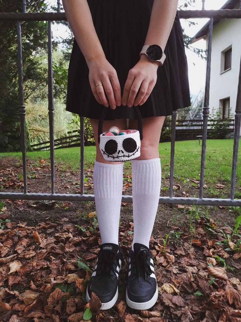 K&ouml;nnte beinhalten: Eine Person tr&auml;gt einen schwarzen Rock, wei&szlig;e Socken und schwarze Sneaker und h&auml;lt einen wei&szlig;en geh&auml;kelten Korb mit einem Jack Skellington Gesicht. Der Korb ist mit bunten S&uuml;&szlig;igkeiten gef&uuml;llt.