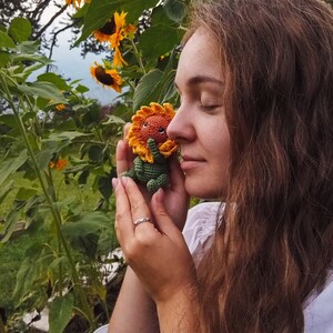 K&ouml;nnte beinhalten: Eine Frau mit langen braunen Haaren h&auml;lt ein geh&auml;keltes Sonnenblumenspielzeug in ihren H&auml;nden. Sie steht auf einem Sonnenblumenfeld.