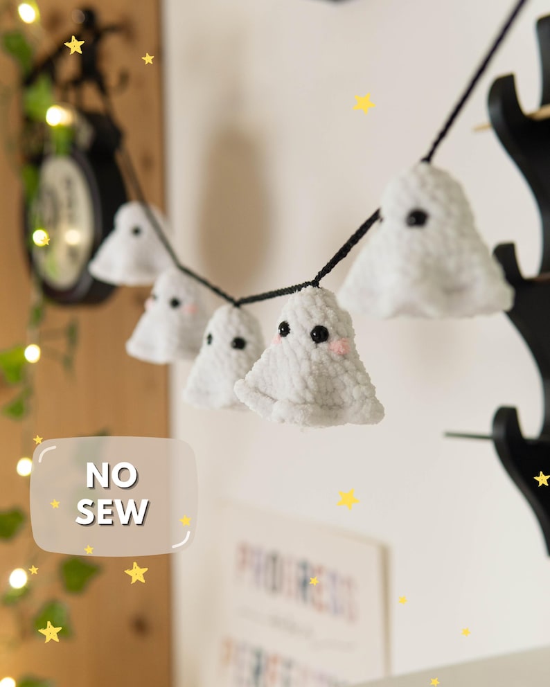 Puede incluir: Una guirnalda de decoraciones de fantasmas blancos y afelpados con ojos negros y mejillas rosadas, ensartadas en un cord&oacute;n negro. Los fantasmas cuelgan sobre un fondo claro, con el texto "NO SEW" en un recuadro blanco. Estrellas amarillas decoran el conjunto.