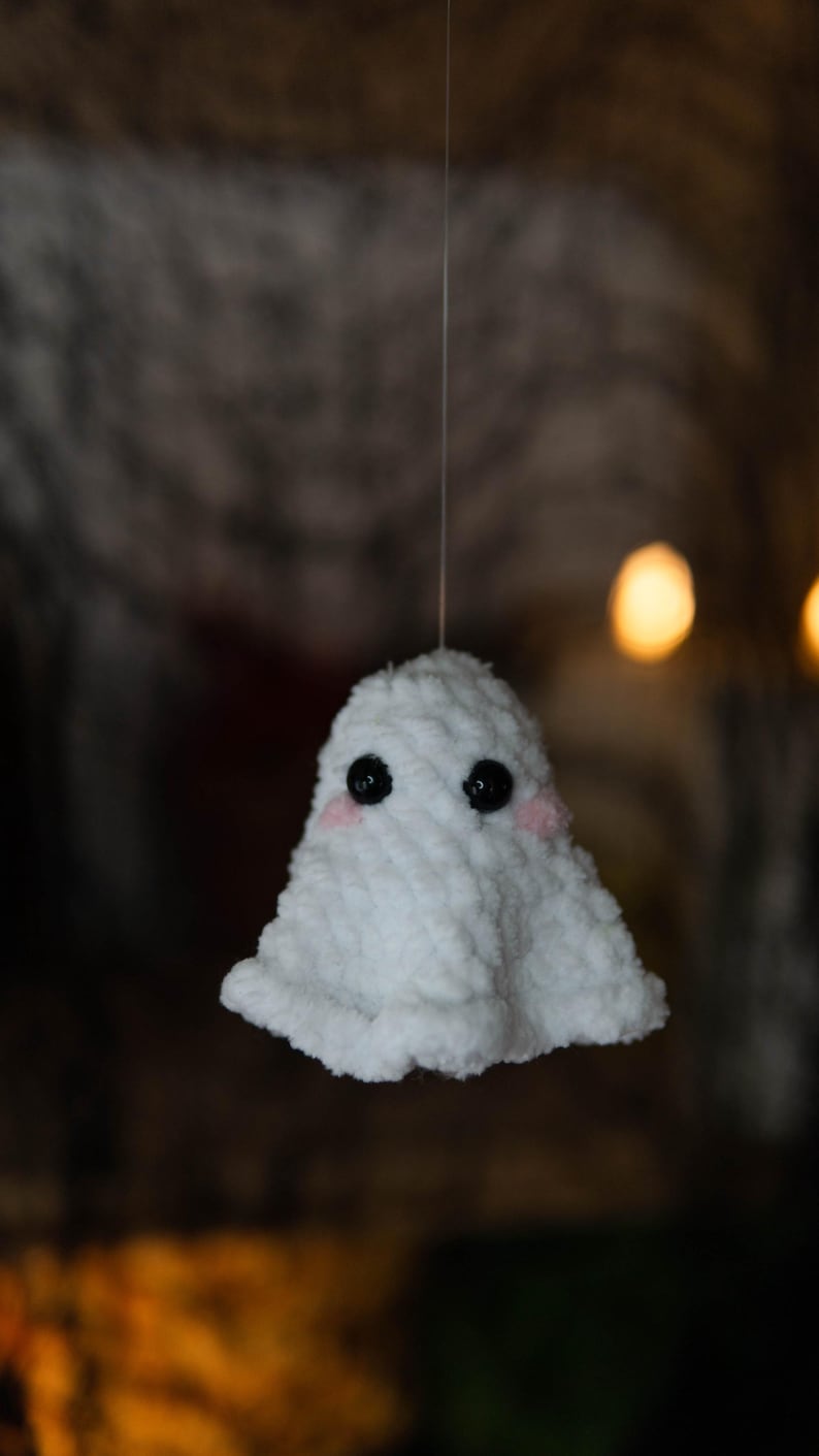 Puede incluir: Un fantasma blanco de ganchillo hecho a mano con ojos de bot&oacute;n negros y mejillas rosadas. El fantasma est&aacute; suspendido por un hilo fino, con un fondo borroso. Esta decoraci&oacute;n caprichosa es perfecta para Halloween o para todo el a&ntilde;o.