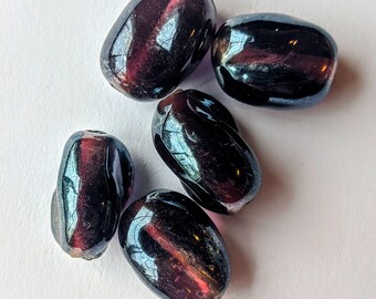 May include: Five iridescent glass beads in shades of purple and black. The beads are oval shaped and have a glossy finish.