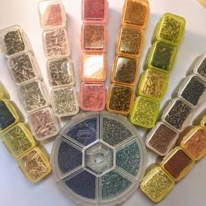 May include: Assortment of small, clear plastic containers filled with colorful beads. The containers are arranged in a hand shape with the containers at the fingertips and the wrist.