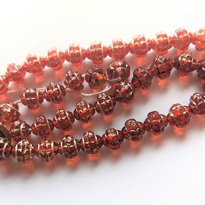 May include: A strand of red glass beads with a white and gold swirl design. The beads are strung on a white thread and have a textured surface. The beads are labeled "Made in China".