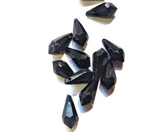 May include: A group of black teardrop-shaped crystal beads. The beads are faceted and have a shiny finish.
