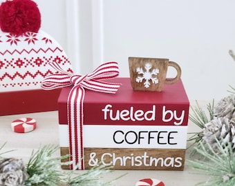 Könnte beinhalten: Ein Holzblock-Schild mit einem rot-weiß-braunen gestreiften Band. Das Schild trägt die Aufschrift "fueled by coffee & christmas" mit einer kleinen Holzkaffeetasse mit einem Schneeflocken-Motiv oben drauf.