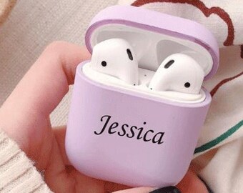 May include: A lilac-colored earbud case with the name "Jessica" printed in black. The case is open, revealing two white earbuds. The case is held in a hand with a black painted fingernail.