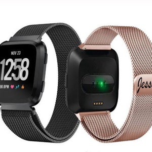 May include: Two smartwatches with black and rose gold mesh bands. One watch displays the time, date, and heart rate. The other watch has a green light and the name "Jessica" engraved on the band.