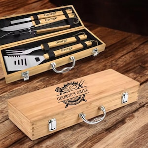 May include: A wooden barbecue tool set with stainless steel utensils, including a spatula, fork, and knife, inside a bamboo case. The case is engraved with "George's Grill" and the name "George" on the tools.