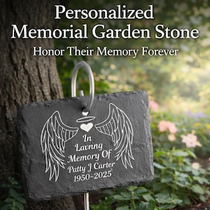 May include: A personalized memorial garden stone with the text "In Loving Memory Of Patty J Carter 1950-2025". The black stone features angel wings and a heart design. The stone is displayed in a garden setting.