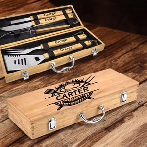 May include: A wooden barbecue tool set in a bamboo case. The case is engraved with "CARTER" and a grill design. Inside, there are stainless steel tools with wooden handles, some engraved with "George".