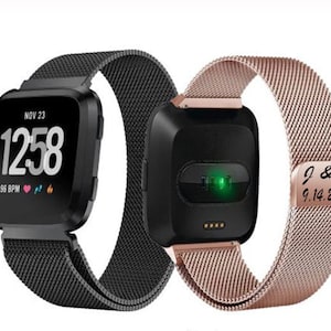 May include: Two smartwatches with black square faces and mesh bands. One watch displays the date, time, and heart rate. The other watch has a rose gold band with engraved initials and a date.