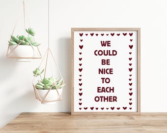 May include: A framed print with the text "WE COULD BE NICE TO EACH OTHER" in burgundy, surrounded by heart shapes. Two hanging planters with succulents are also in the image.