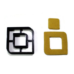 May include: A black plastic cookie cutter shaped like a square with a smaller square inside. The cutter is shown next to a cookie that has been cut with the cutter.