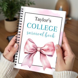 May include: A spiral-bound notebook with a cover that reads "Taylor's COLLEGE survival book." The cover features a watercolor illustration of a pink bow against a soft pink watercolor background. The notebook is held open by a person.