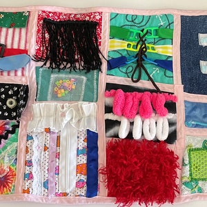 May include: A multi-colored fabric activity mat with various textures and features for sensory play. It includes a zipper, buttons, buckles, laces, and a variety of fabrics.