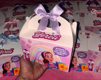 May include: White party favour box with a purple bow and the name "Yereli" in pink. The box features a cartoon illustration of a girl, a rainbow, and the text "Hi Friends! Can You Say Happy Birthday YERELI!"
