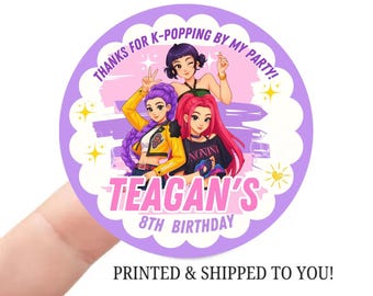May include: A round sticker with a purple scalloped edge features three cartoon figures. The text "THANKS FOR K-POPPING BY MY PARTY!" arches across the top. Below, the text "TEAGAN'S 8TH BIRTHDAY" is displayed in pink. The sticker is held by a finger.