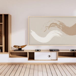 May include: A modern living room with a light wood entertainment center and a large framed abstract art piece. The artwork features brushstrokes in white and brown against a beige background. The room has a minimalist design.